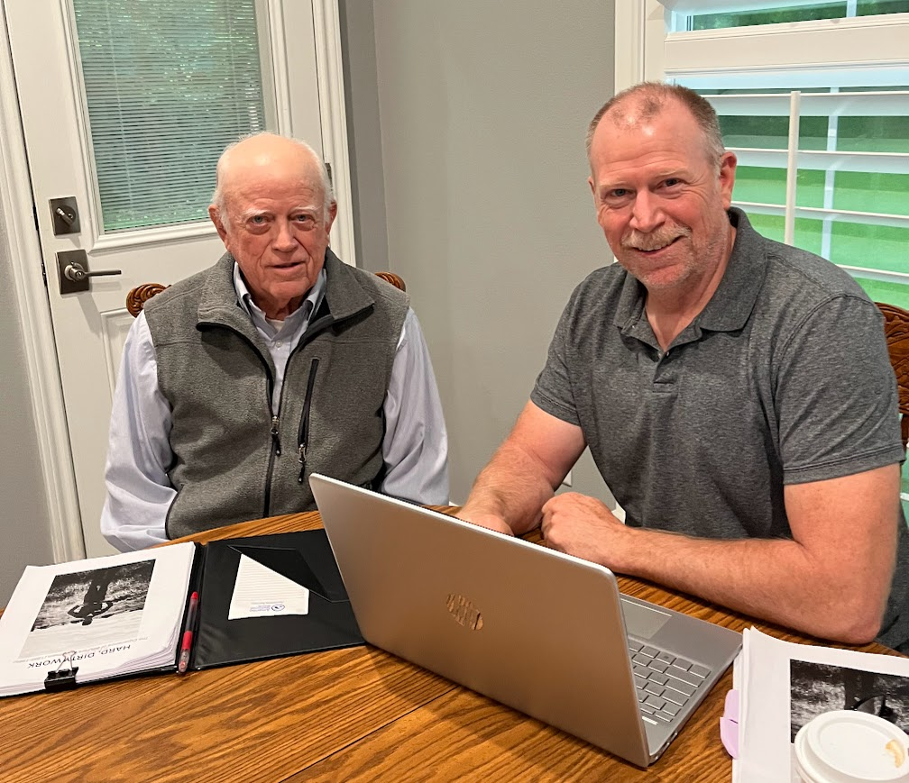 Bill and his son Theron seated at a table with a laptop and the book manuscript